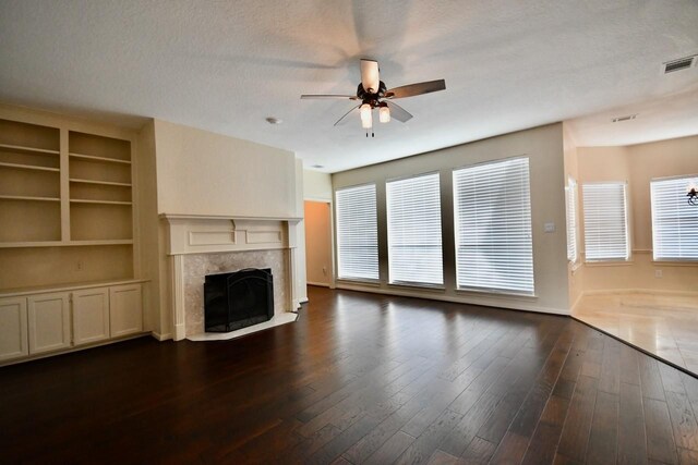 unfurnished living room featuring dark wood-type flooring, ceiling fan, plenty of natural light, and a premium fireplace