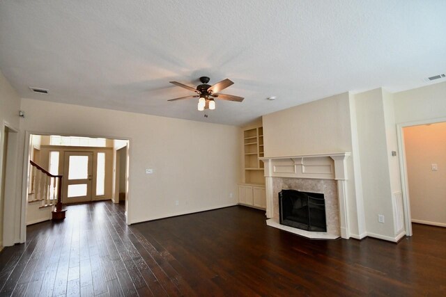 unfurnished living room with built in shelves, dark wood-type flooring, a premium fireplace, and ceiling fan