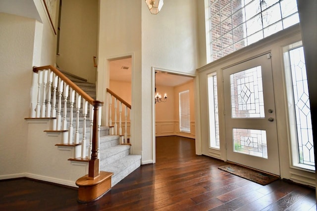 foyer entrance featuring an inviting chandelier, a towering ceiling, and dark hardwood / wood-style floors