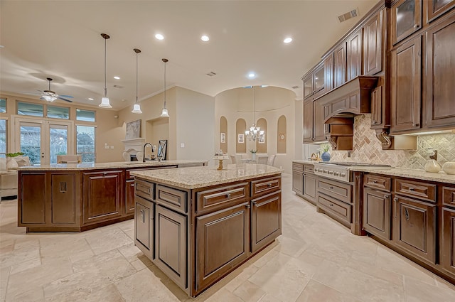 kitchen with a center island, decorative light fixtures, stainless steel gas cooktop, and arched walkways