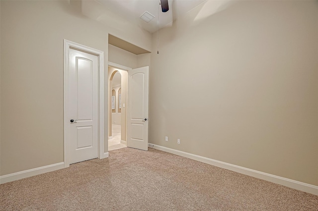 unfurnished bedroom featuring carpet floors, arched walkways, baseboards, and a ceiling fan