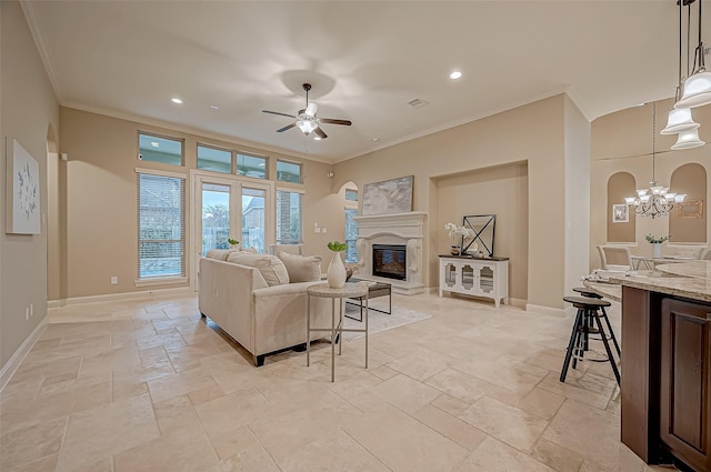 living area with stone tile floors, baseboards, a glass covered fireplace, crown molding, and ceiling fan with notable chandelier