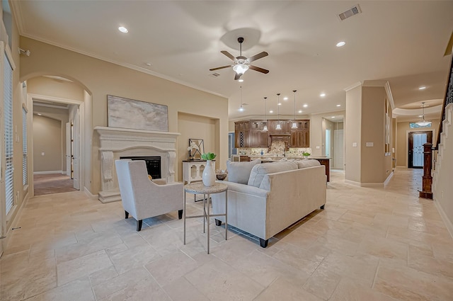 living area featuring baseboards, visible vents, a fireplace with raised hearth, arched walkways, and ornamental molding