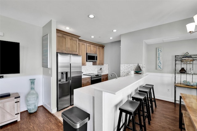 kitchen with a breakfast bar area, dark hardwood / wood-style flooring, decorative backsplash, kitchen peninsula, and stainless steel appliances