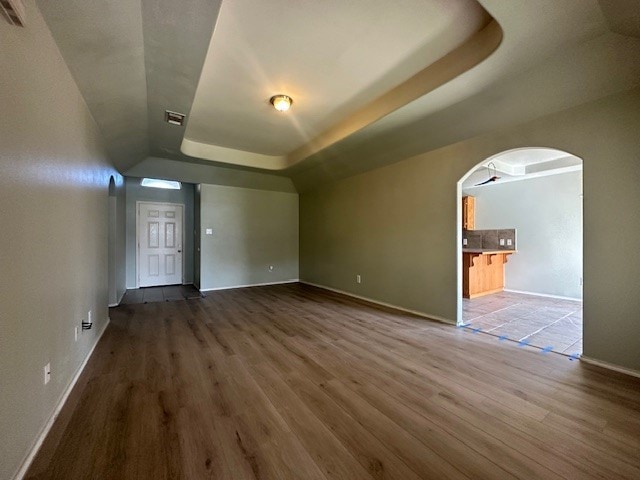 unfurnished living room with wood-type flooring and a tray ceiling