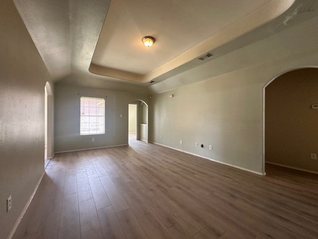 empty room with wood-type flooring and a tray ceiling