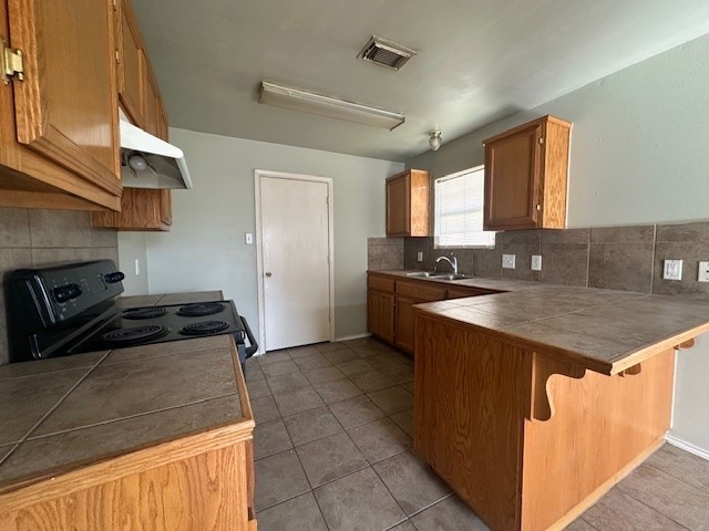 kitchen with sink, electric range oven, a kitchen breakfast bar, tile counters, and kitchen peninsula