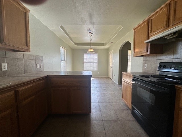 kitchen featuring black electric range, hanging light fixtures, a tray ceiling, kitchen peninsula, and backsplash