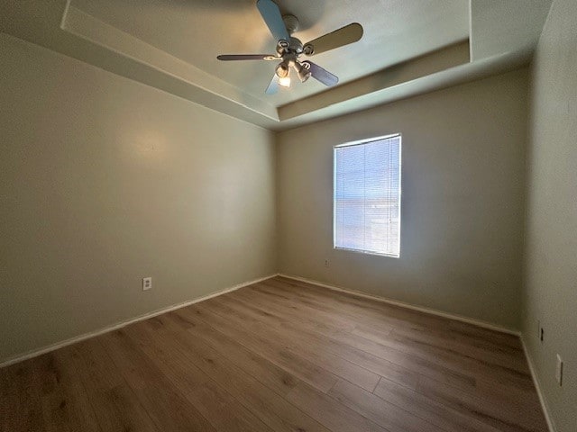 empty room with ceiling fan, a tray ceiling, and hardwood / wood-style floors