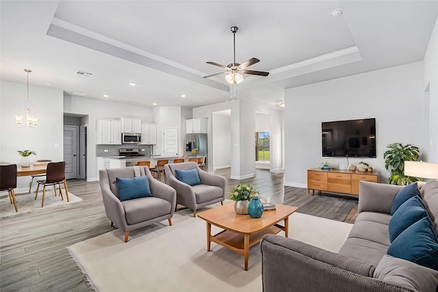 living room featuring crown molding, ceiling fan with notable chandelier, light hardwood / wood-style floors, and a raised ceiling