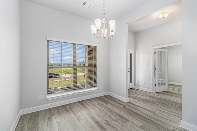 unfurnished dining area featuring an inviting chandelier and light hardwood / wood-style flooring