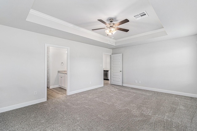 unfurnished bedroom featuring ensuite bathroom, ornamental molding, a raised ceiling, and light carpet