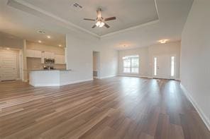 unfurnished living room featuring dark wood-type flooring, ceiling fan, and a tray ceiling