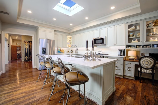 kitchen with appliances with stainless steel finishes, sink, white cabinets, a kitchen island with sink, and a raised ceiling