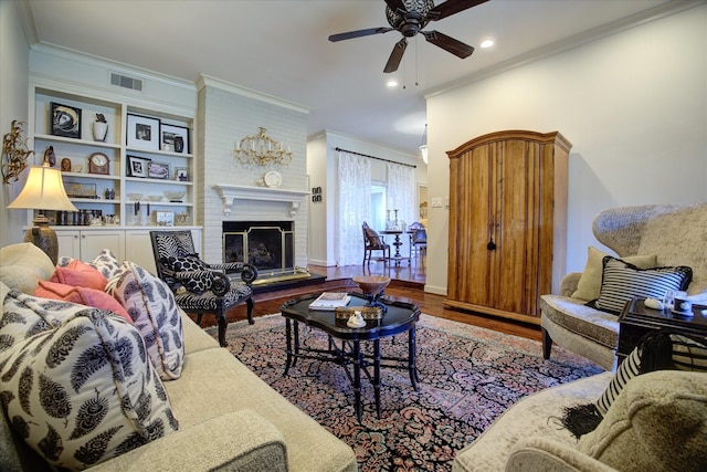 living room featuring wood-type flooring, a brick fireplace, ornamental molding, and ceiling fan