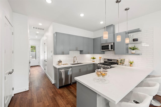 kitchen featuring sink, appliances with stainless steel finishes, dark hardwood / wood-style flooring, kitchen peninsula, and pendant lighting