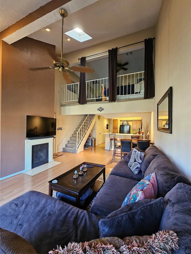 living room featuring hardwood / wood-style floors, a towering ceiling, a skylight, and ceiling fan