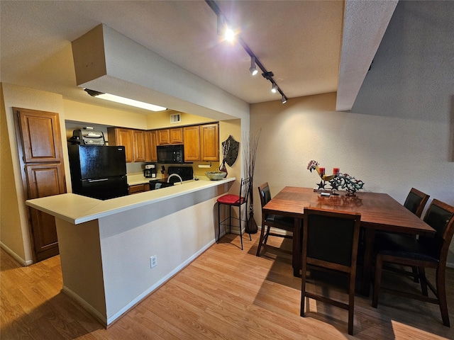 kitchen featuring sink, light hardwood / wood-style flooring, a kitchen breakfast bar, kitchen peninsula, and black appliances