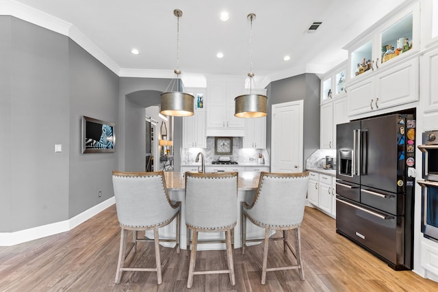 kitchen with pendant lighting, white cabinetry, a kitchen island with sink, light stone counters, and high end black fridge