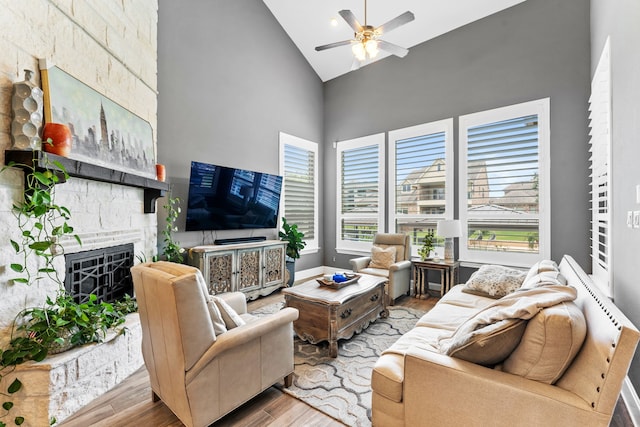 living room with ceiling fan, high vaulted ceiling, a fireplace, and light wood-type flooring