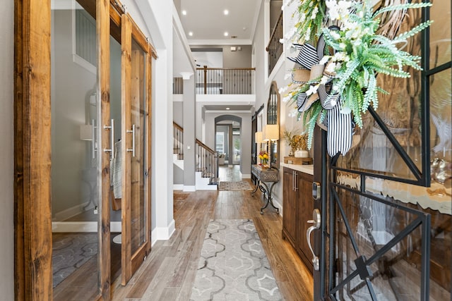 foyer with crown molding, arched walkways, wood finished floors, stairs, and baseboards