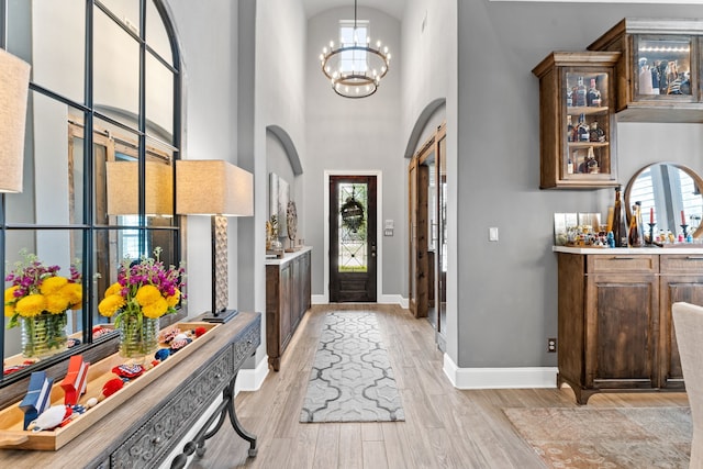 foyer entrance featuring light wood finished floors, baseboards, arched walkways, and an inviting chandelier