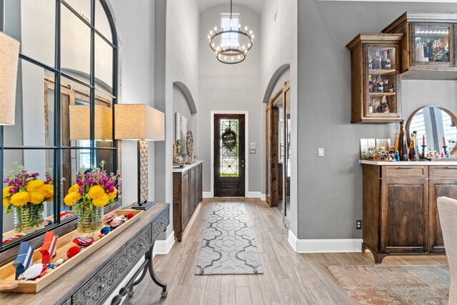 foyer entrance with baseboards, light wood finished floors, an inviting chandelier, and a healthy amount of sunlight