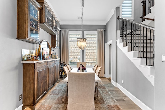 dining area featuring dark wood-type flooring, indoor bar, crown molding, and a notable chandelier