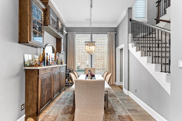 dining room featuring light wood-type flooring, an inviting chandelier, baseboards, crown molding, and stairs