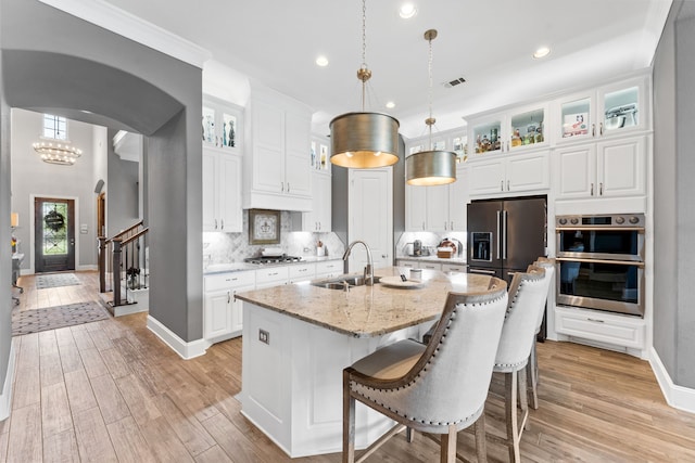 kitchen featuring arched walkways, light wood finished floors, visible vents, a sink, and fridge with ice dispenser