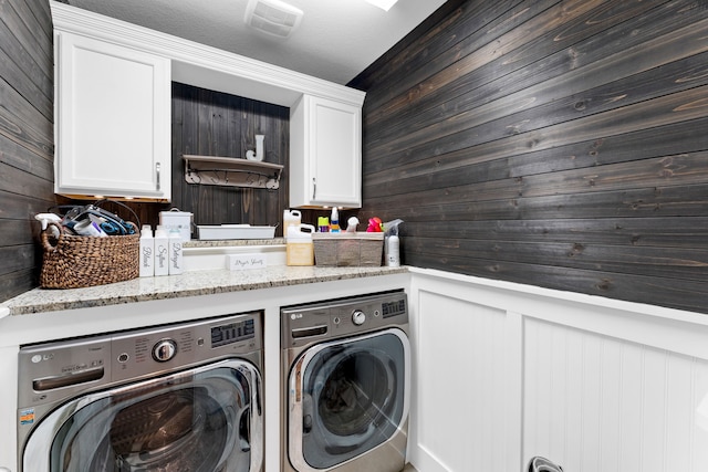 laundry room featuring cabinet space, washing machine and dryer, visible vents, and wood walls