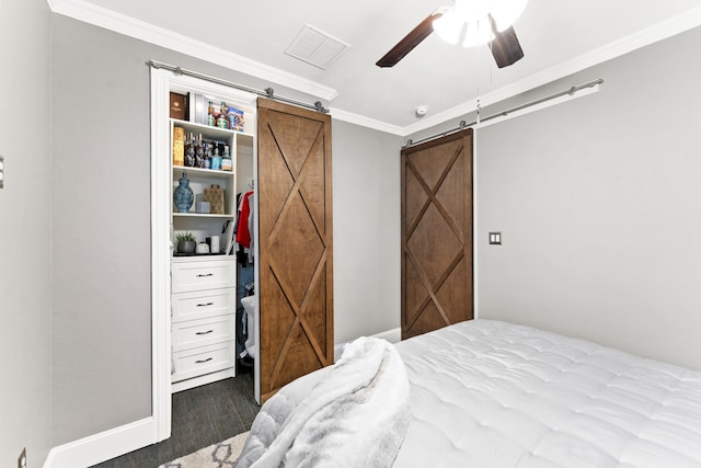 bedroom featuring visible vents, a barn door, ornamental molding, a ceiling fan, and wood finished floors