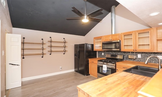 kitchen featuring butcher block countertops, sink, appliances with stainless steel finishes, light hardwood / wood-style floors, and vaulted ceiling