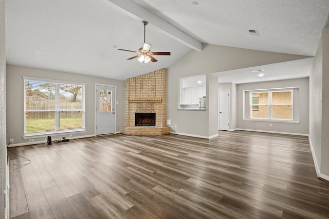 unfurnished living room featuring beamed ceiling, ceiling fan, a brick fireplace, and dark hardwood / wood-style flooring