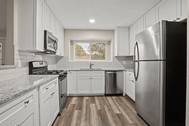 kitchen with white cabinetry, sink, decorative backsplash, light hardwood / wood-style floors, and stainless steel appliances