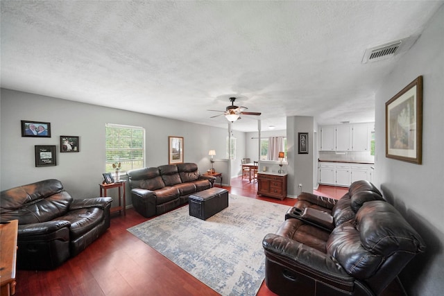 living area featuring dark wood-style floors, visible vents, a textured ceiling, and a ceiling fan