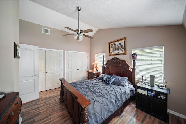 bedroom featuring visible vents, dark wood-type flooring, two closets, a ceiling fan, and vaulted ceiling