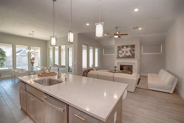 kitchen featuring an island with sink, sink, stainless steel dishwasher, and decorative light fixtures