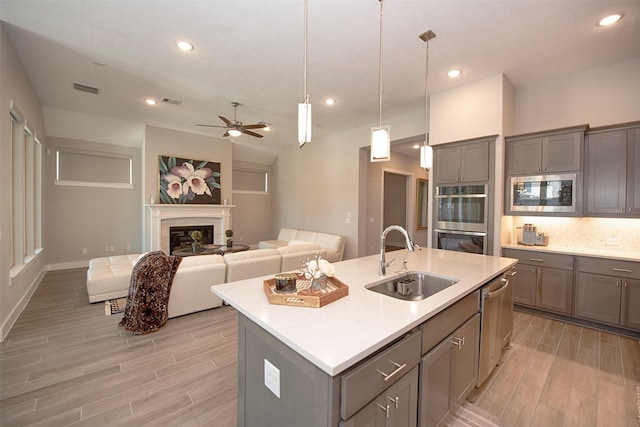 kitchen featuring appliances with stainless steel finishes, pendant lighting, an island with sink, sink, and light hardwood / wood-style floors