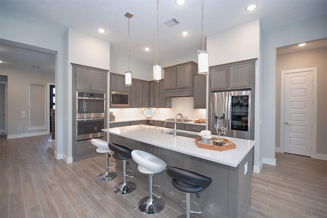 kitchen with a breakfast bar area, decorative light fixtures, a center island with sink, appliances with stainless steel finishes, and decorative backsplash