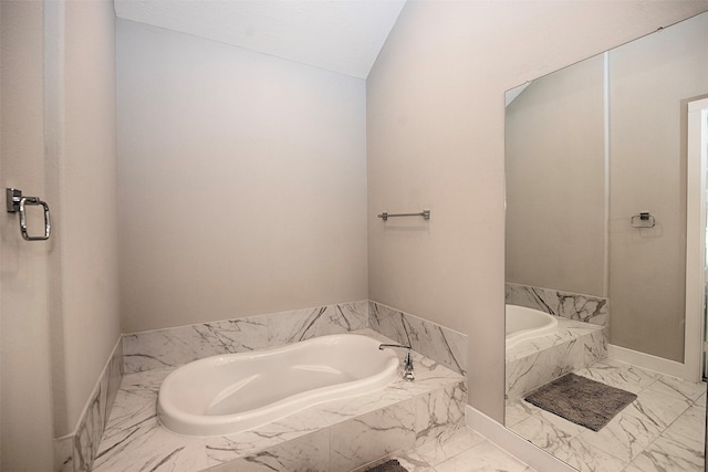 bathroom featuring lofted ceiling and tiled tub