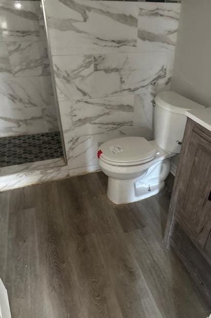 bathroom featuring wood-type flooring, toilet, vanity, and a tile shower