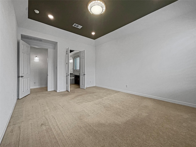 unfurnished bedroom featuring ensuite bath, a tray ceiling, and light carpet