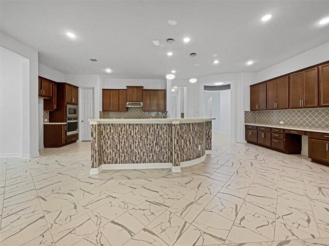 kitchen with stainless steel appliances, a center island, built in desk, and backsplash