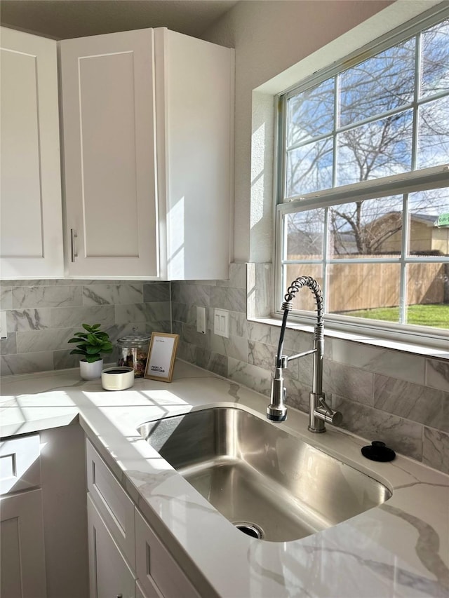 kitchen featuring light stone countertops, plenty of natural light, white cabinets, and a sink