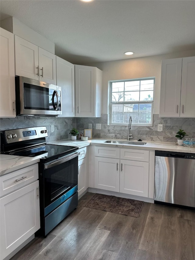 kitchen with dark wood-style floors, stainless steel appliances, decorative backsplash, white cabinetry, and a sink