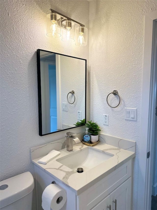 bathroom with a textured wall, vanity, and toilet