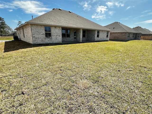 rear view of property with brick siding, roof with shingles, and a yard