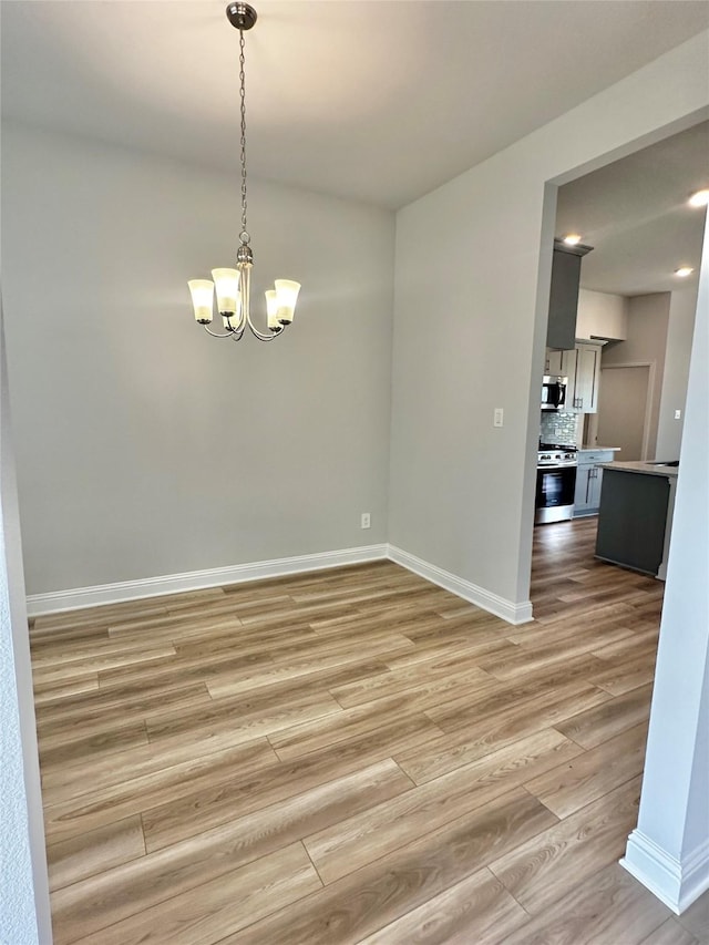 spare room with light wood finished floors, an inviting chandelier, and baseboards