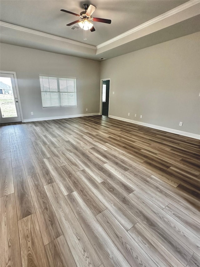 empty room with ceiling fan, wood finished floors, baseboards, ornamental molding, and a raised ceiling